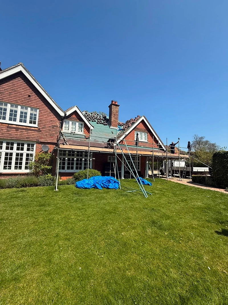 Workers repairing the roof of a red brick house under clear blue sky with scaffolding set up.