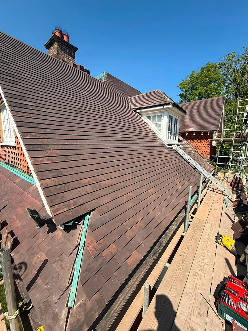 Newly installed brown tiled roof with scaffolding and a ladder under bright blue sky.