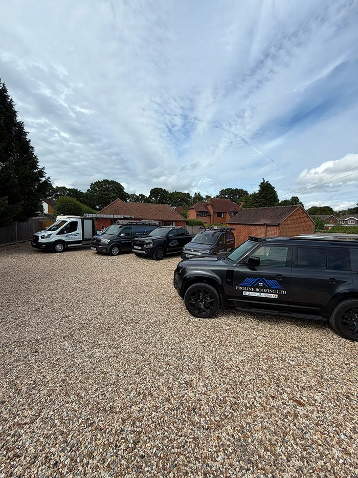Five company vehicles parked on gravel in front of suburban houses under a partly cloudy sky.