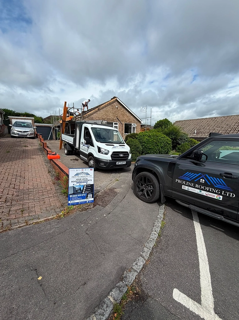 Workers on roof of suburban brick house with Proline Roofing Ltd vehicles and sign in driveway.