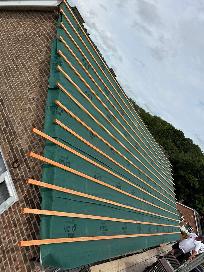 Roof under construction with green weatherproof membrane and evenly spaced wooden battens.