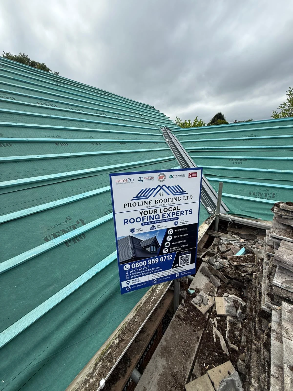 Roof under construction with green waterproof membrane and a Proline Roofing Ltd sign with contact info.