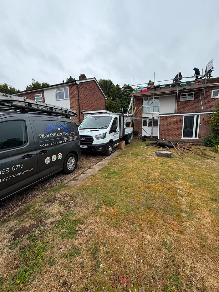 Workers on roof of a brick house with Proline Roofing vans and scaffolding in front yard.