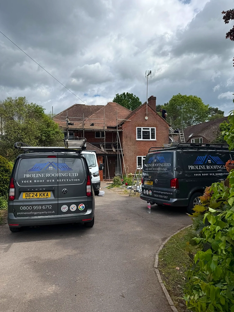 Two Proline Roofing vans parked on driveway of brick house with scaffolding under cloudy sky.
